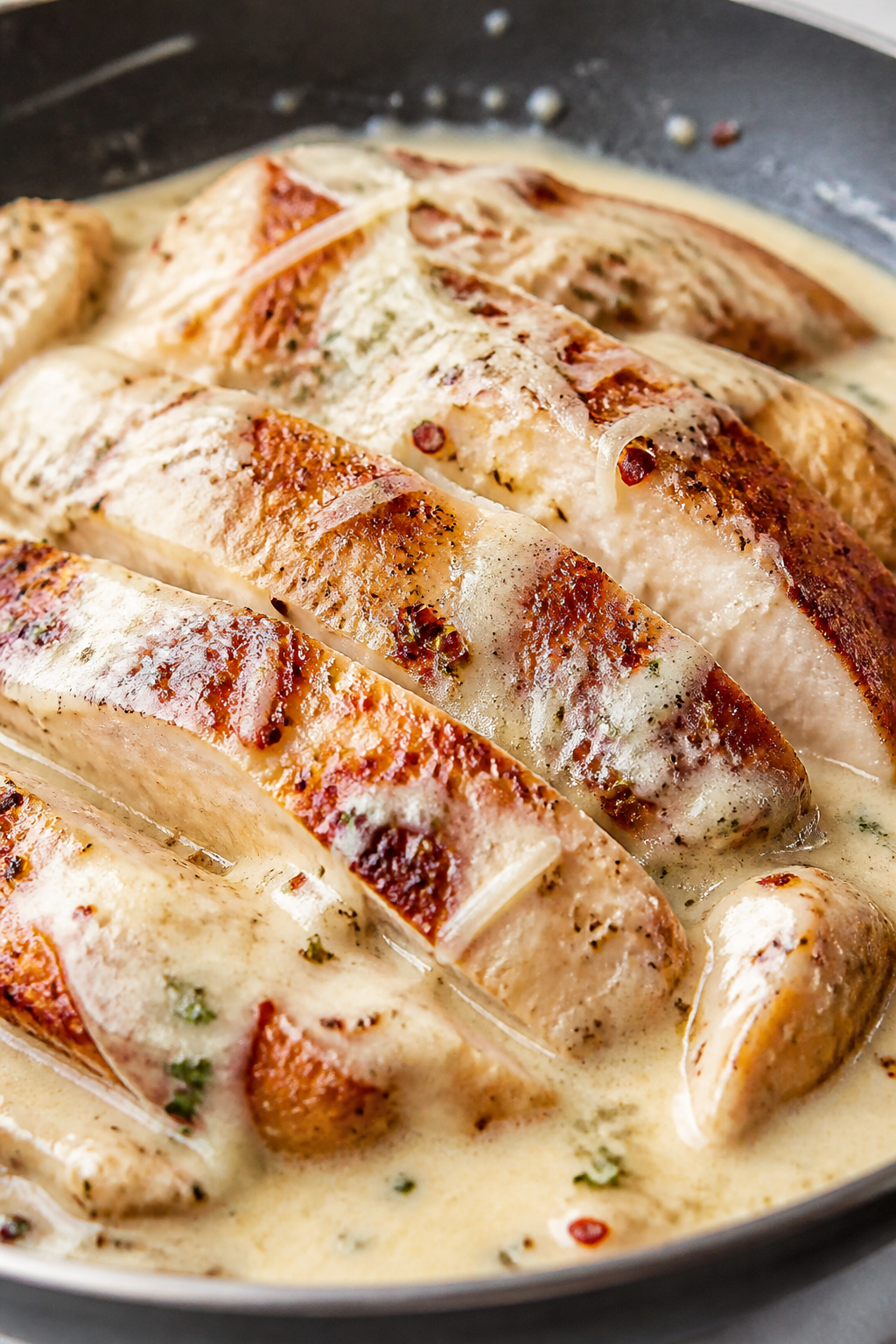 Close-up detail: Sliced, golden-seared chicken breast tossed in silky Alfredo sauce in a skillet, sa