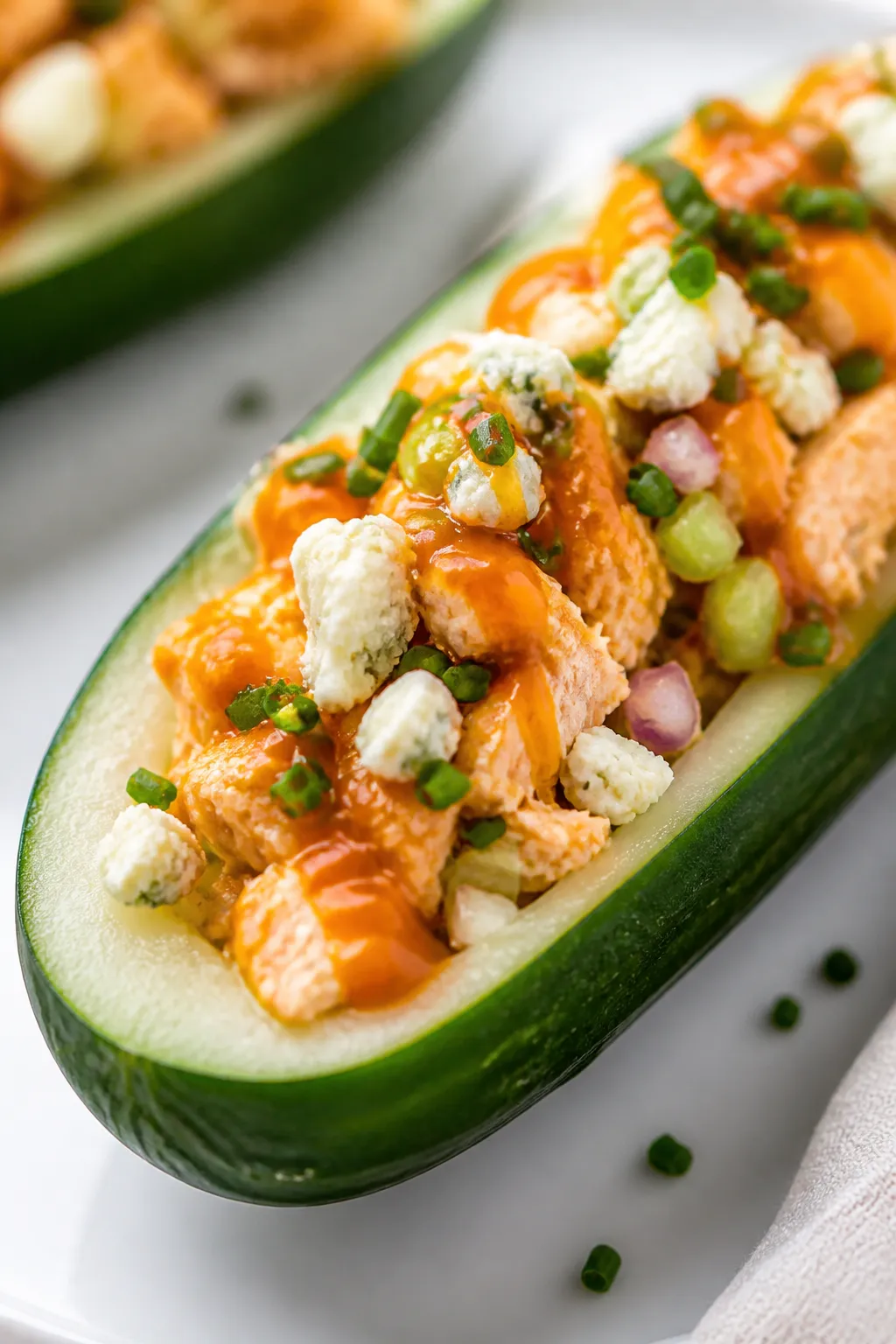 Close-up detail: A freshly assembled Buffalo Chicken Cucumber Boat, the creamy orange-tinted Buffalo