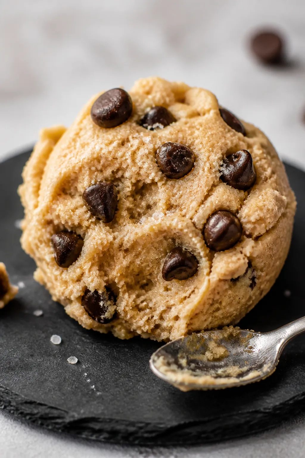Close-up detail: A scoop of keto chocolate chip protein dough on a matte slate plate, showcasing glo