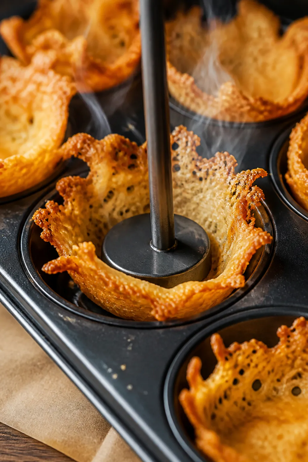 Close-up detail shot: Freshly baked cheese rounds being molded into taco cups in a muffin tin, edges