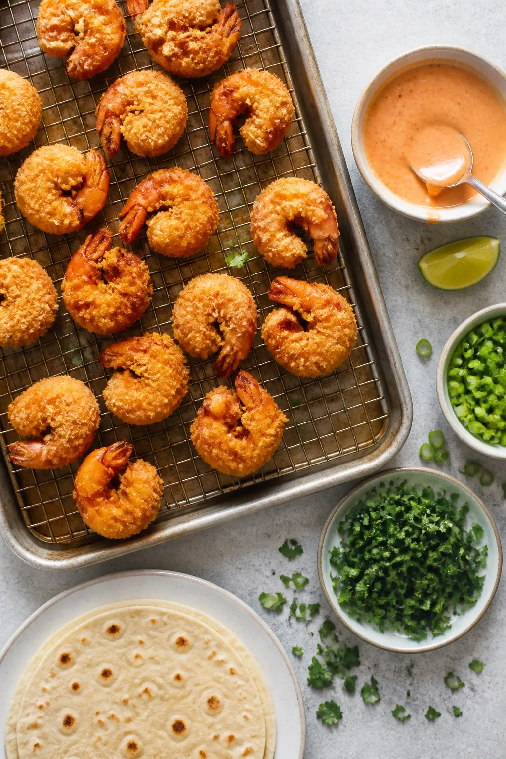 Cooking process: Overhead shot of freshly fried shrimp draining on a wire rack over a sheet pan, per